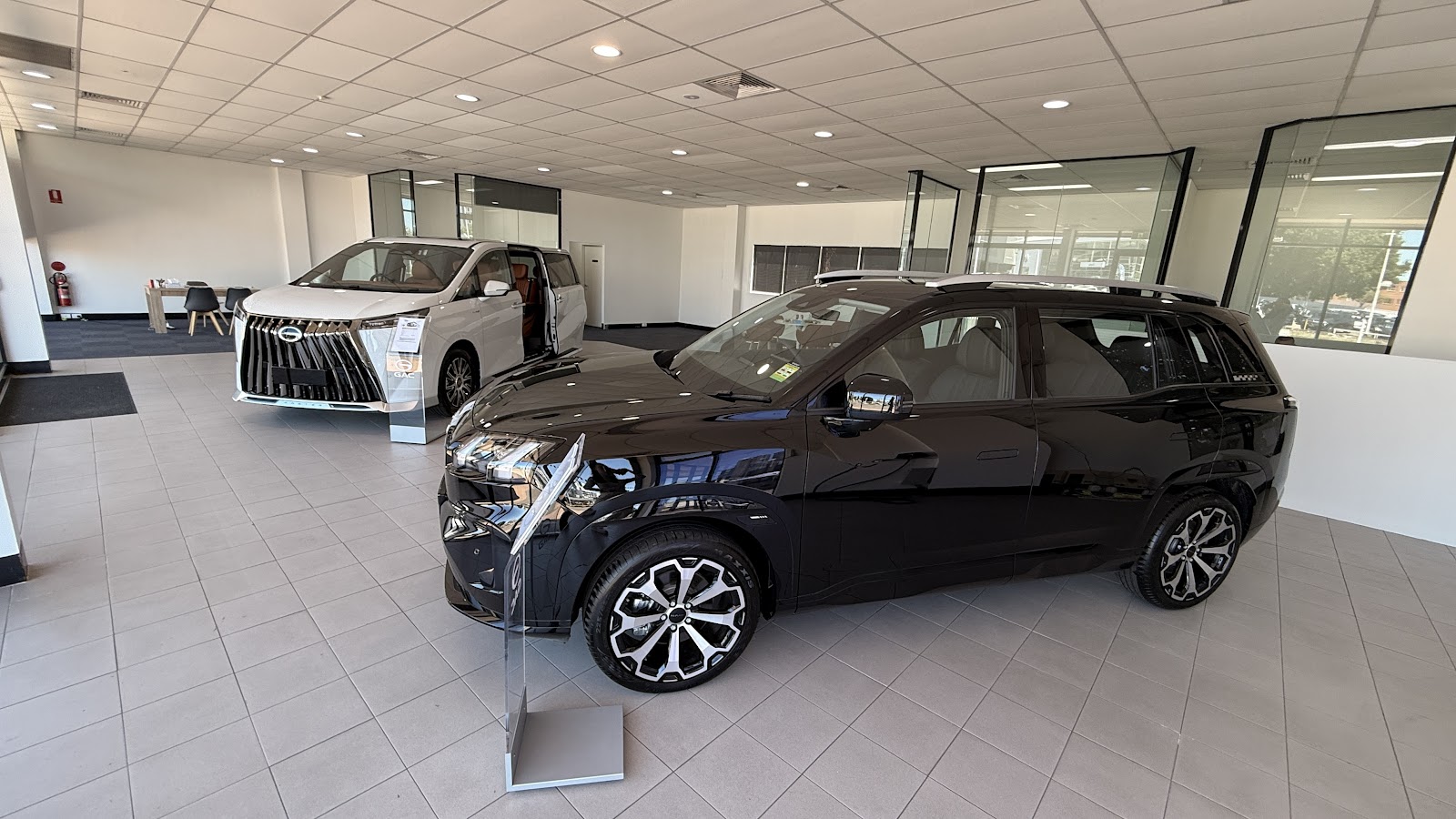 The Aion Parramatta GAC showroom floor, a black Aion V in the foreground and a white M8 people mover behind it.